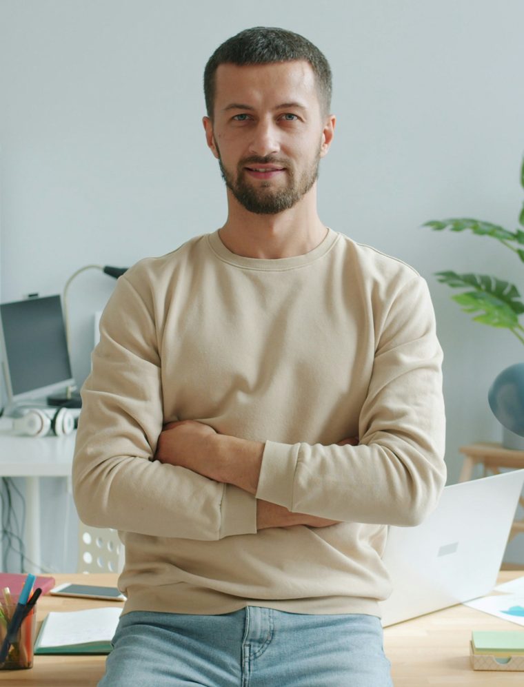 A business owner in his office, sitting on his desk with arms crossed